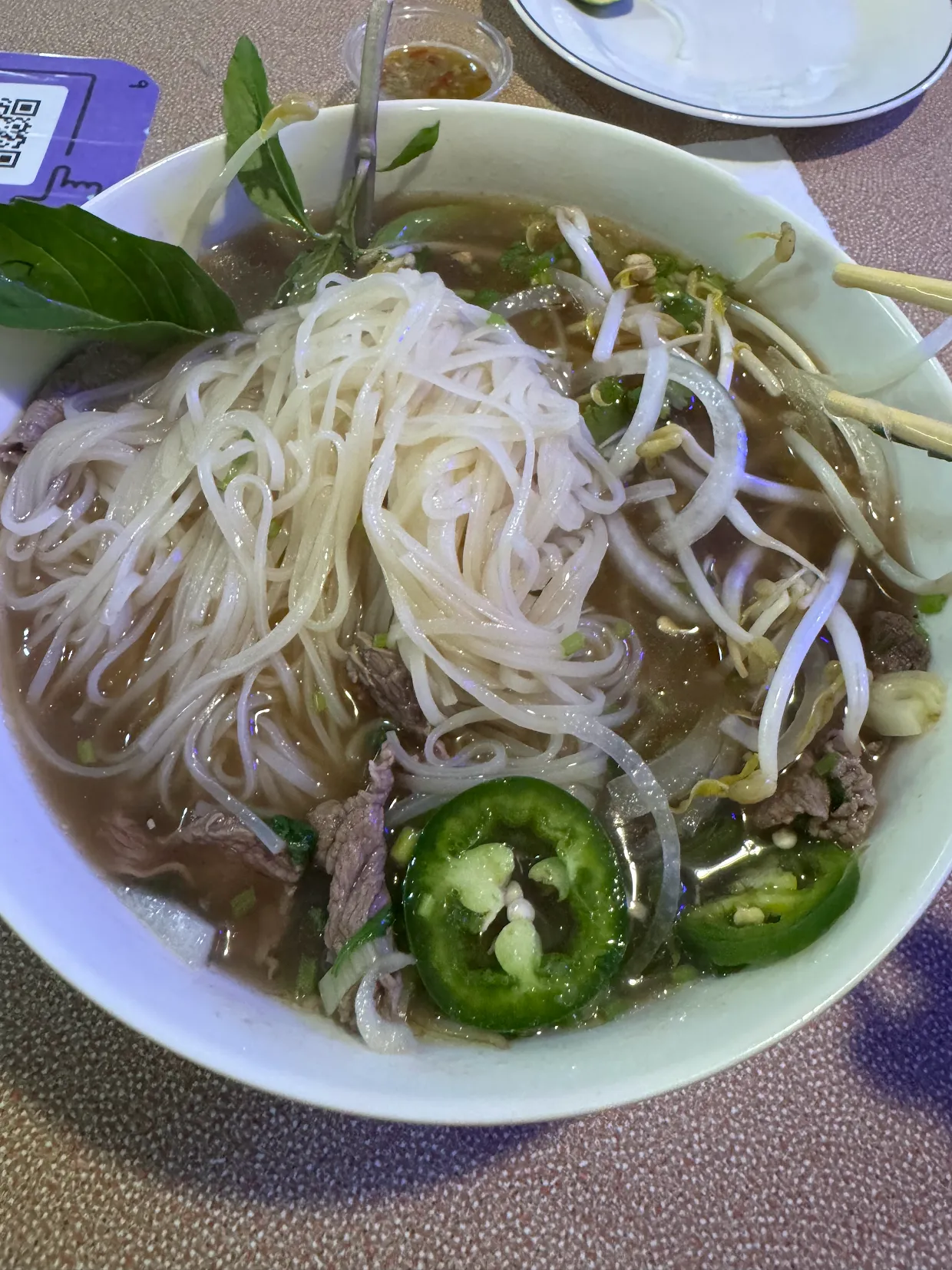 A steaming bowl of Kathiew: rice noodles, tender beef, Thai basil, and jalapeño in the house broth
